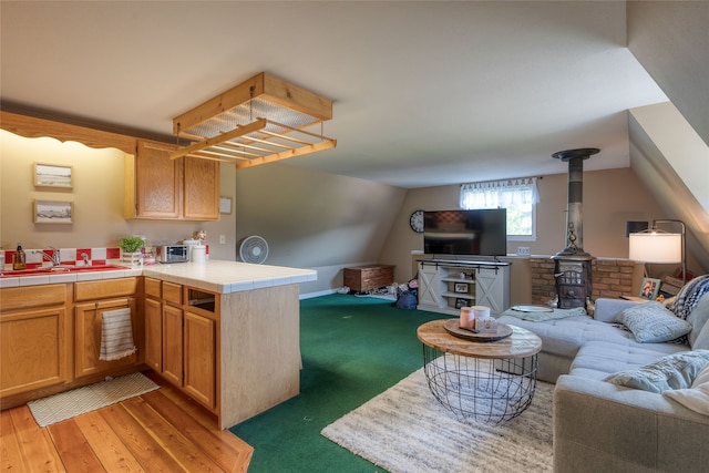 kitchen with sink, dark colored carpet, tile countertops, kitchen peninsula, and a wood stove