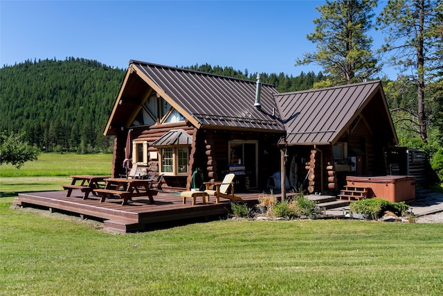 rear view of house featuring a hot tub, a wooden deck, and a lawn