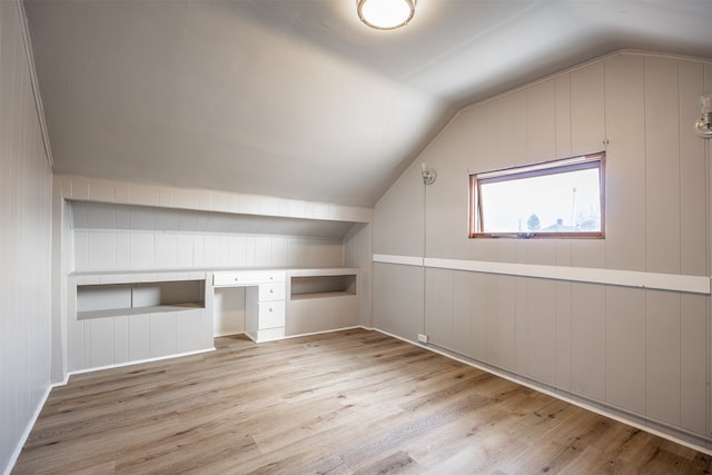 additional living space featuring vaulted ceiling, light hardwood / wood-style flooring, wooden walls, and built in desk