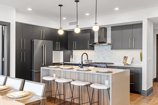 kitchen with pendant lighting, a kitchen bar, wall chimney range hood, stainless steel appliances, and a center island with sink