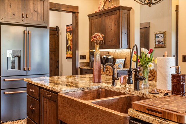 kitchen with tasteful backsplash, dark brown cabinets, high end refrigerator, and light stone counters