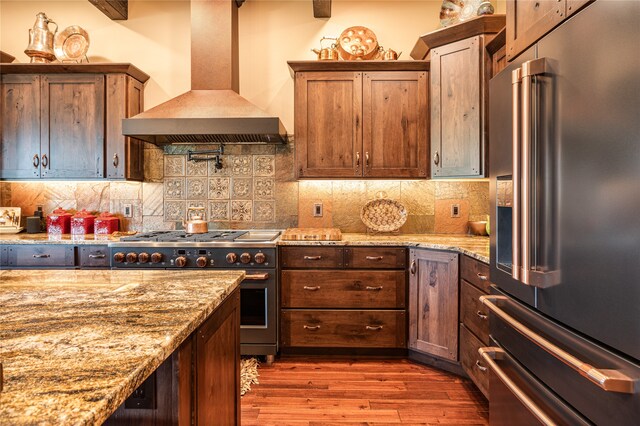 kitchen with hardwood / wood-style floors, high quality appliances, wall chimney range hood, and backsplash