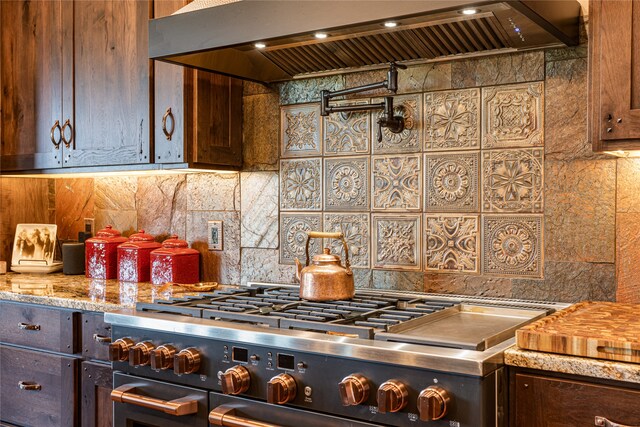 kitchen with dark brown cabinets, light stone countertops, premium range hood, tasteful backsplash, and high end stainless steel range