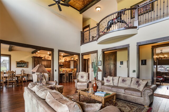 living room with ceiling fan with notable chandelier, beam ceiling, dark hardwood / wood-style floors, and a high ceiling