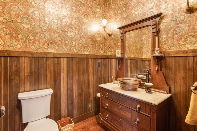 bathroom with wood walls, wood-type flooring, toilet, and vanity