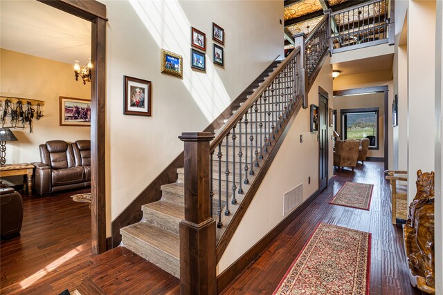 stairway featuring dark wood-type flooring, a towering ceiling, and a notable chandelier