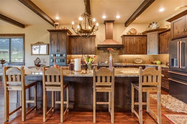 kitchen with light stone counters, dark hardwood / wood-style flooring, beam ceiling, stainless steel appliances, and premium range hood