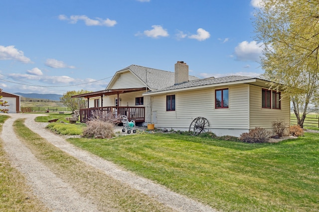 rear view of house with an outdoor structure, a yard, a garage, and a wooden deck