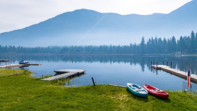 view of dock featuring a view of trees, a water and mountain view, and a yard