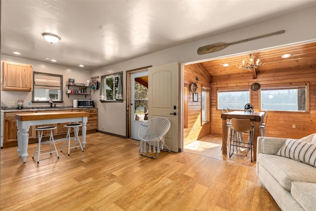 kitchen featuring sink, a breakfast bar area, wood walls, an inviting chandelier, and light hardwood / wood-style floors