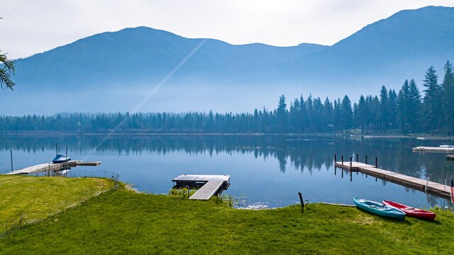 view of dock with a water and mountain view and a lawn