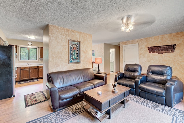 living room with sink, ceiling fan, light wood-type flooring, and a textured ceiling