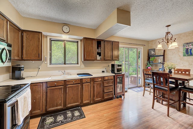 kitchen with a textured ceiling, electric range oven, light hardwood / wood-style floors, decorative light fixtures, and an inviting chandelier