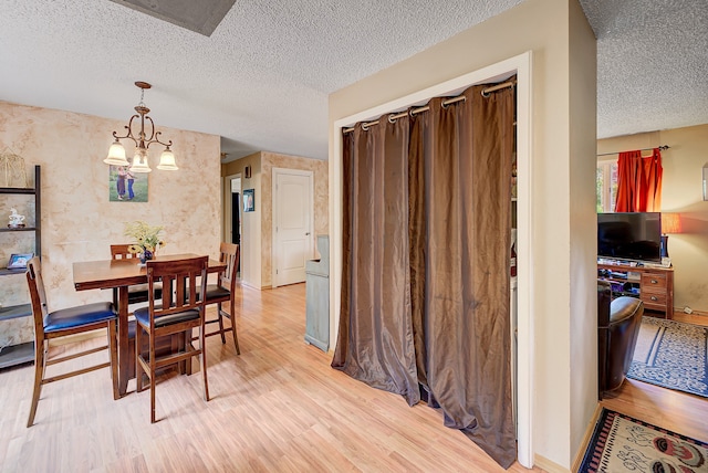 dining space with a notable chandelier, a textured ceiling, and light wood-type flooring