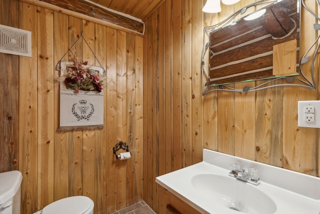 bathroom featuring toilet, vanity, and wood walls