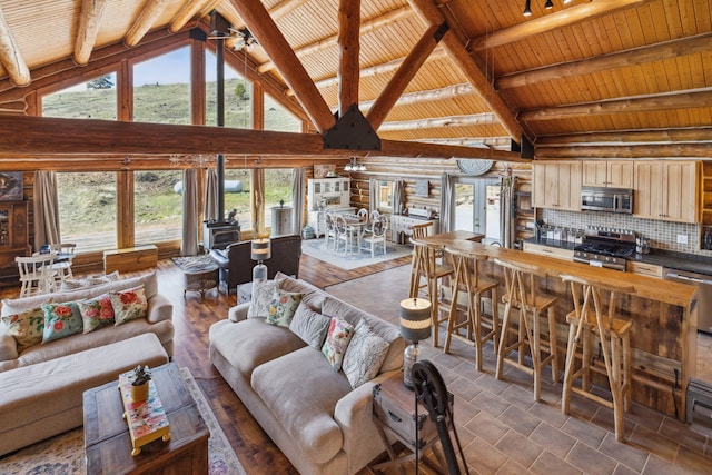 living room with log walls, high vaulted ceiling, wooden ceiling, beamed ceiling, and a wood stove