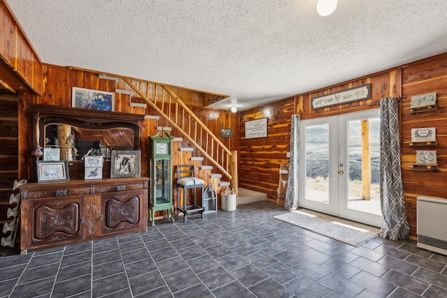 foyer entrance with french doors, a textured ceiling, and wooden walls