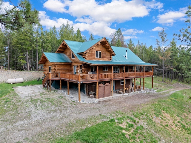 rear view of house with driveway, a garage, log exterior, metal roof, and a deck