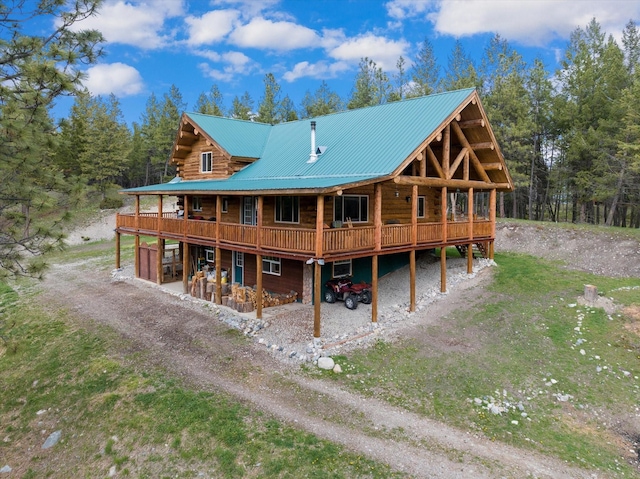 back of house featuring a garage, dirt driveway, log exterior, metal roof, and a deck