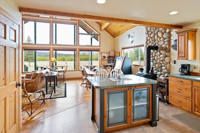 400 Kintla Ranch Rd, Polebridge, MT 59928 - kitchen with beamed ceiling, dark countertops, a wood stove, a center island, and brown cabinetry