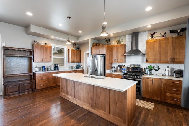 kitchen with dark hardwood / wood-style floors, a kitchen island with sink, wall chimney range hood, appliances with stainless steel finishes, and decorative light fixtures