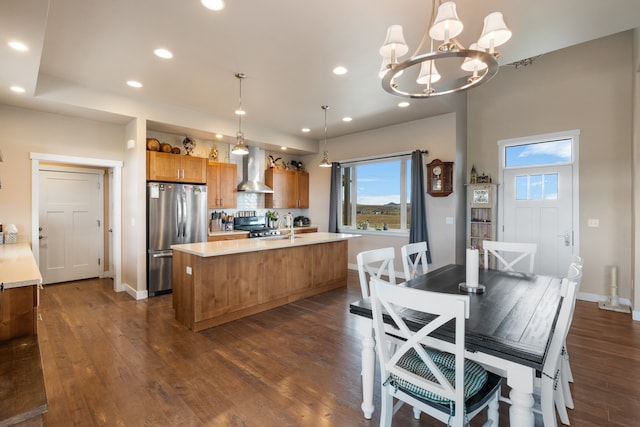 kitchen featuring hanging light fixtures, a center island with sink, wall chimney exhaust hood, dark wood-type flooring, and appliances with stainless steel finishes