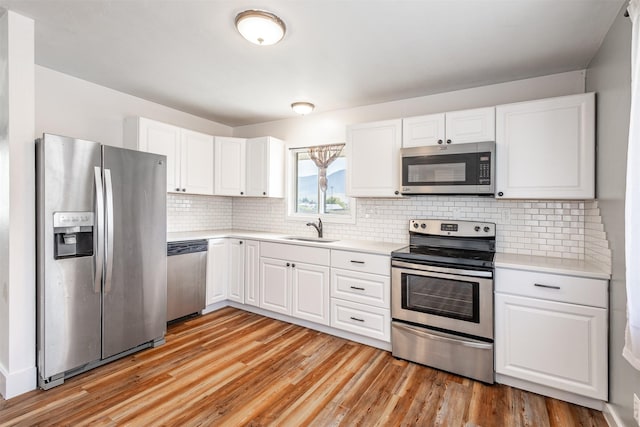 kitchen with appliances with stainless steel finishes, white cabinetry, sink, decorative backsplash, and light wood-type flooring