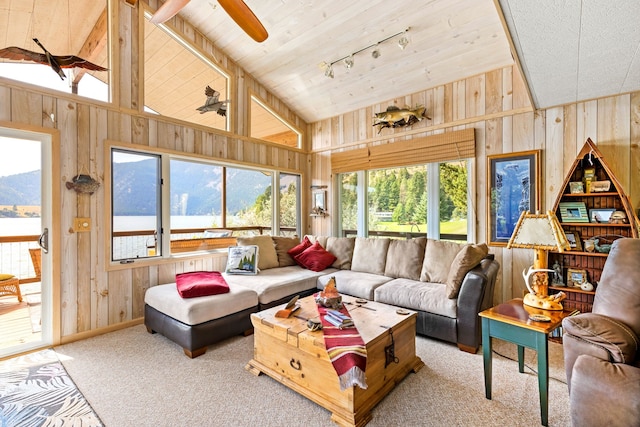 carpeted living room featuring wood walls, high vaulted ceiling, a water and mountain view, rail lighting, and ceiling fan