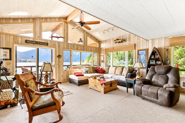 carpeted living room with ceiling fan, vaulted ceiling, a water and mountain view, and wooden walls