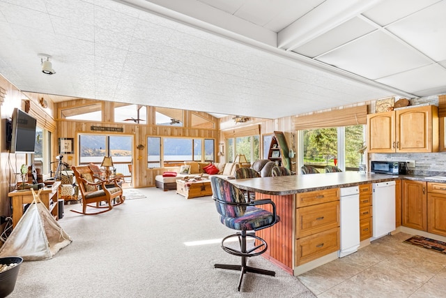 kitchen featuring light colored carpet, a kitchen breakfast bar, dishwasher, and wooden walls