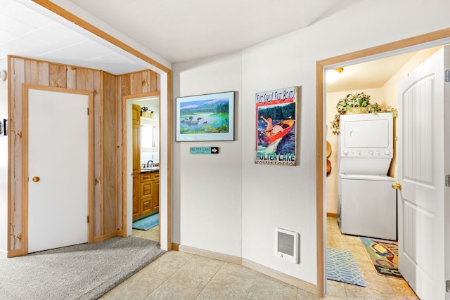 hallway with light carpet, sink, wooden walls, and stacked washer and dryer