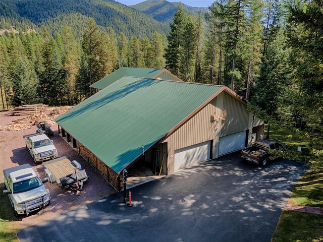 exterior space featuring a detached garage, an outdoor structure, metal roof, a wooded view, and a mountain view