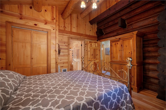 bedroom with beamed ceiling, a closet, wood finished floors, wood walls, and log walls