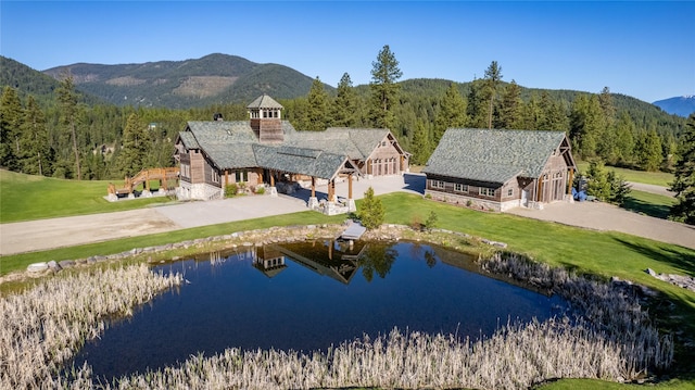 rear view of property featuring a yard, driveway, a wooded view, and a water and mountain view