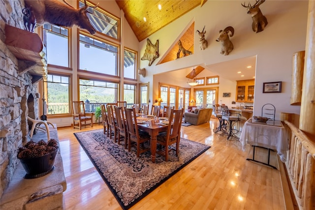 dining area with high vaulted ceiling, a large fireplace, plenty of natural light, and light wood finished floors