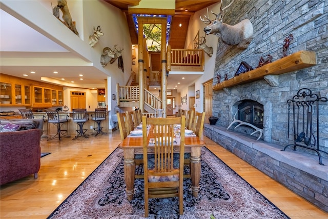 dining area featuring stairs, a fireplace, a towering ceiling, and light wood-style flooring