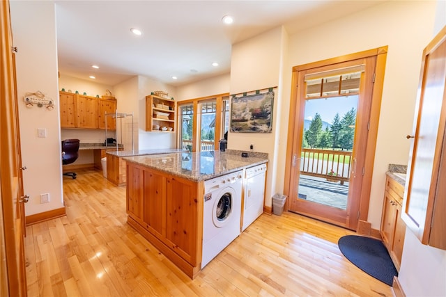 kitchen with light stone counters, built in desk, washing machine and clothes dryer, open shelves, and light wood-style floors