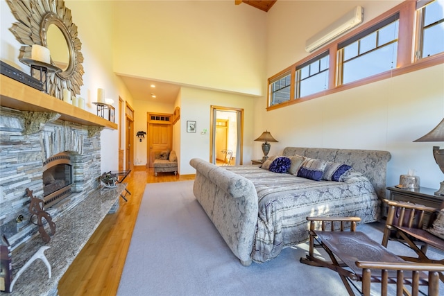 bedroom featuring a wall unit AC, a fireplace, wood finished floors, and a towering ceiling