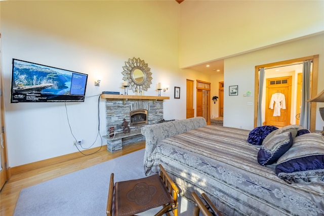 bedroom featuring a fireplace, light wood-style flooring, and a towering ceiling