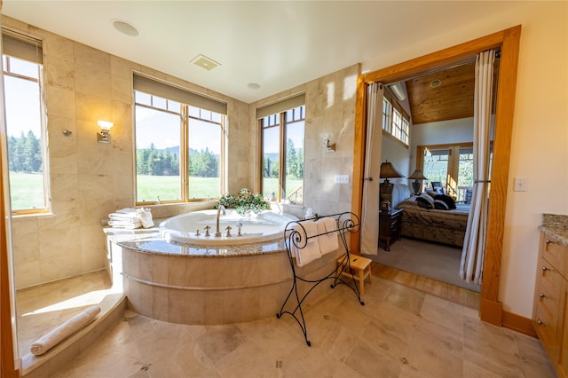 ensuite bathroom featuring a wealth of natural light, vanity, and tile walls