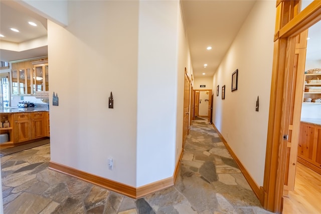 hallway featuring baseboards, stone tile flooring, and recessed lighting