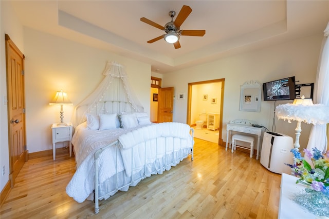 bedroom featuring light wood-type flooring, a raised ceiling, connected bathroom, and baseboards