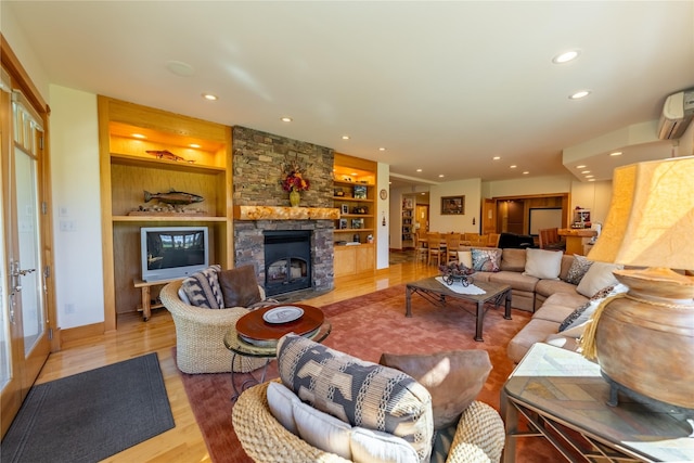 living room featuring light wood finished floors, built in features, a wall mounted AC, a fireplace, and recessed lighting