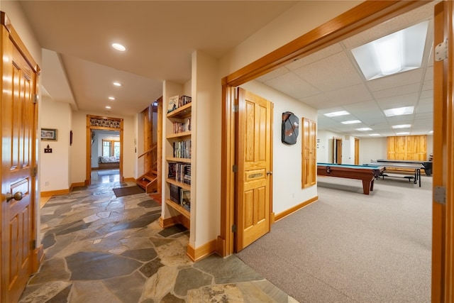 hallway featuring a paneled ceiling, baseboards, stone finish floor, and recessed lighting