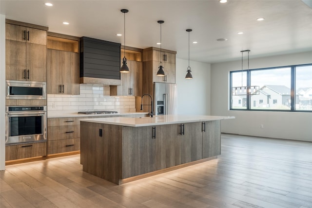 209 Mannington St, Kalispell, MT 59901 - kitchen with stainless steel appliances, modern cabinets, ventilation hood, light wood finished floors, and brown cabinets