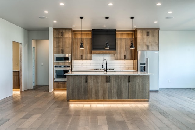 209 Mannington St, Kalispell, MT 59901 - kitchen with appliances with stainless steel finishes, a center island with sink, light countertops, backsplash, and light wood-style flooring