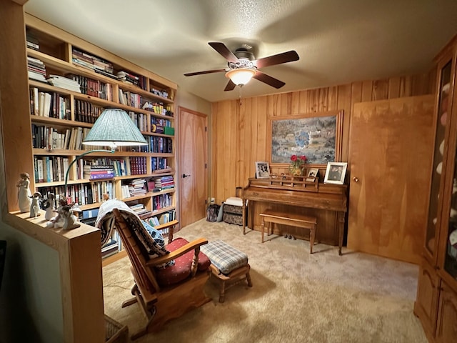 sitting room with ceiling fan, wood walls, and light carpet