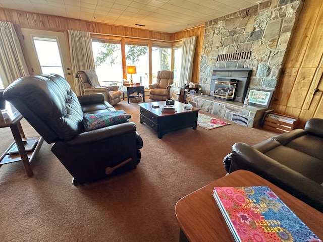 living room featuring carpet, a stone fireplace, and wooden walls