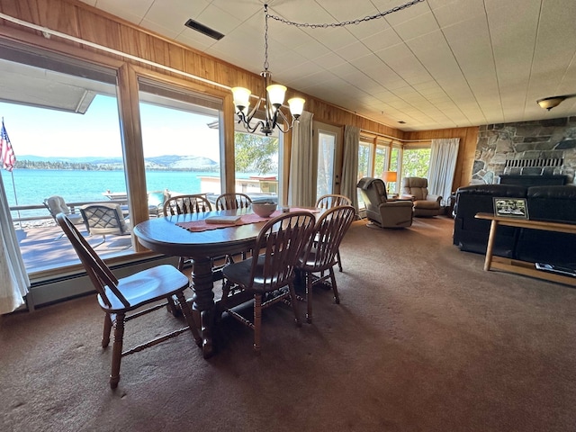 dining area featuring a healthy amount of sunlight, a water view, a chandelier, and dark carpet