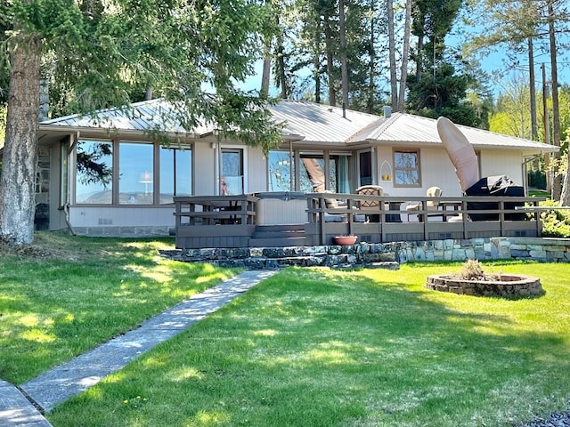 rear view of property with a lawn, a wooden deck, a hot tub, and a fire pit